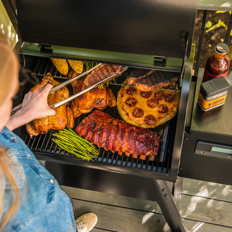 Frau grillt Fleisch und Gemüse auf einem Traeger Pro D2 575 Pelletgrill