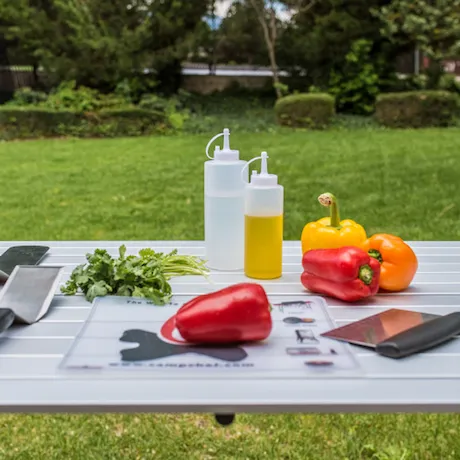 Das Toolset von Camp Chef auf einer Wiese mit Paprikas, Öl und Petersilie bedeckt.