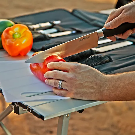 Mann schneidet rote Paprika mit Messer. Das Profi-Messerset von Camp Chef im Hintergrund. 