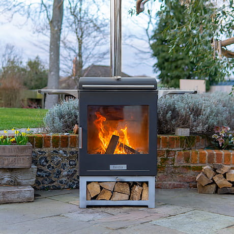 Ein Outdoorkamin mit Holzfeuer auf einer Terrasse mit Holzlagemöglichkeit unter dem Kamin