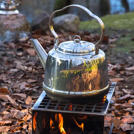 Edelstahl-Teekessel auf einem kleinen Outdoor-Grill mit Flammen darunter