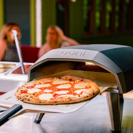 Pizza im Ooni Pizzaofen, im Hintergrund zwei Personen