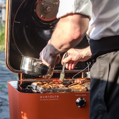 Everdure Holzkohlegrill mit Koch beim Grillen