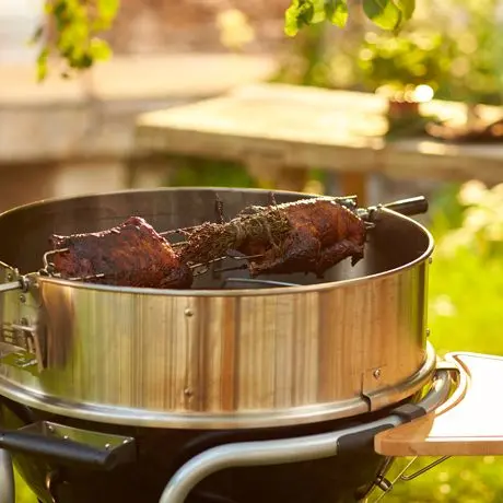 Grillspieß mit Braten, der über einem Grillgerät im Garten rotiert