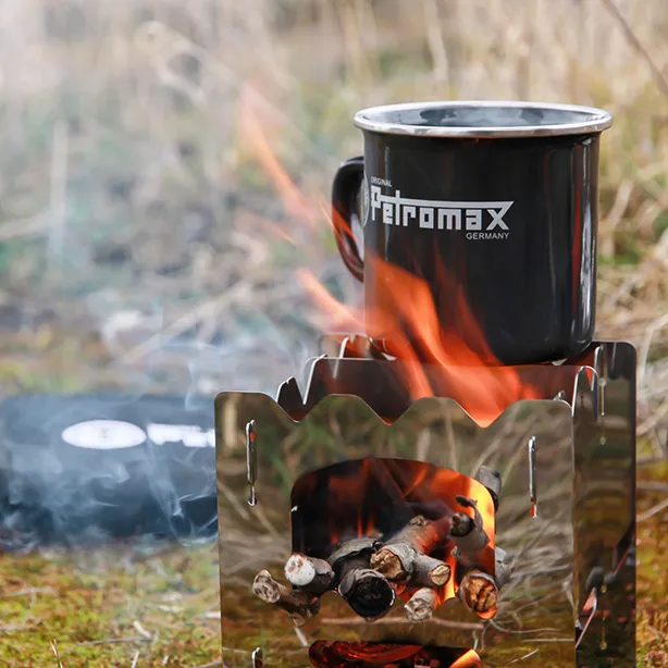 Kleiner Outdoor-Holzofen mit brennendem Feuer und Petromax-Tasse