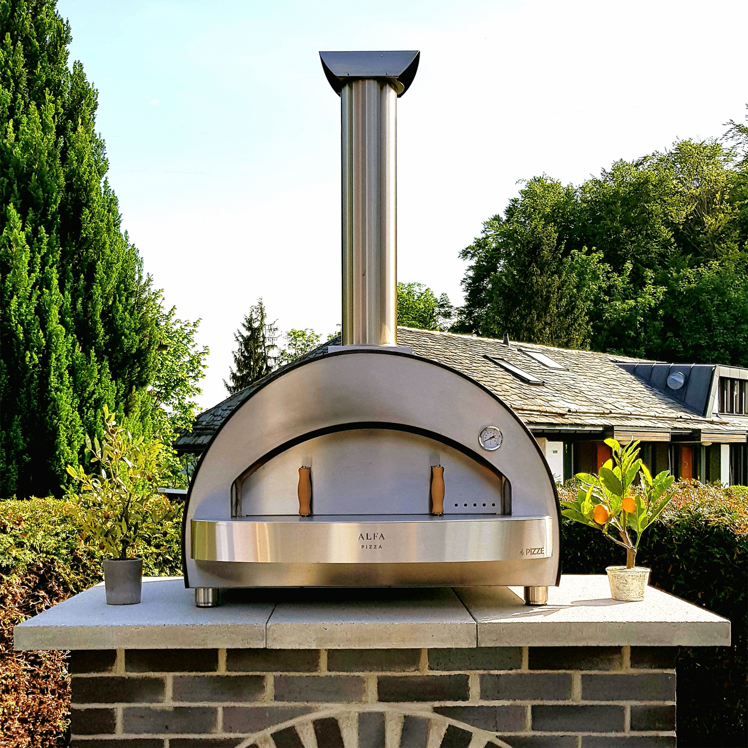 Alfa Pizzaofen auf einem Steintisch mit Pflanzen im Garten