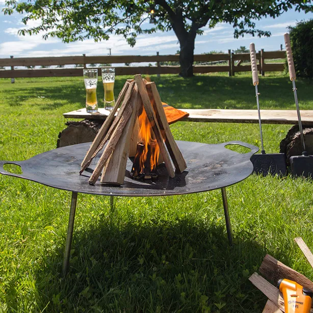 Feuerschale im Freien mit brennendem Holz und Getränken im Hintergrund