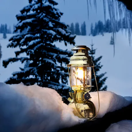 Goldene Laterne auf einem verschneiten Geländer, mit schneebedeckten Bäumen im Hintergrund