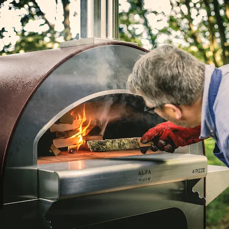 Mann legt Holz in einen Alfa Pizzaofen im Freien