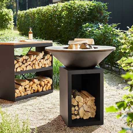 Ein eleganter moderner Grillbereich im Garten mit einem großen runden Grill und einem Holzlagerregal.