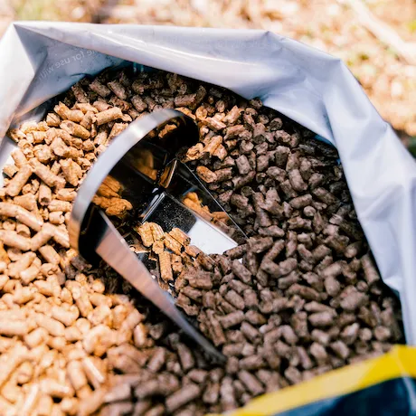 Eine geöffnete Tüte mit Grillpellets, in der eine Metallschaufel steckt.