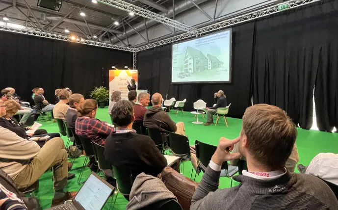 viele-personen-sitzen-und-hören-einem-vortrag-in-der-messehalle-zu