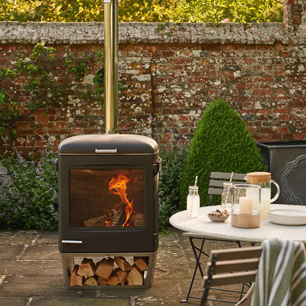 Outdoor-Ofen mit brennendem Feuer und Holzstapeln darunter auf einer Terrasse