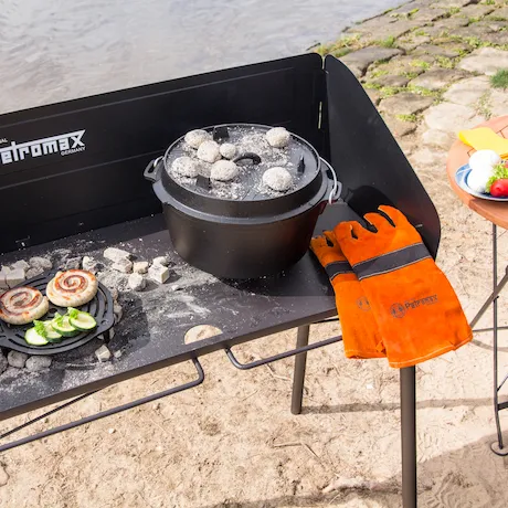 Feuertopf auf einem Petromax Feuertopftisch am Strand, mit Handschuhen und Grillgut